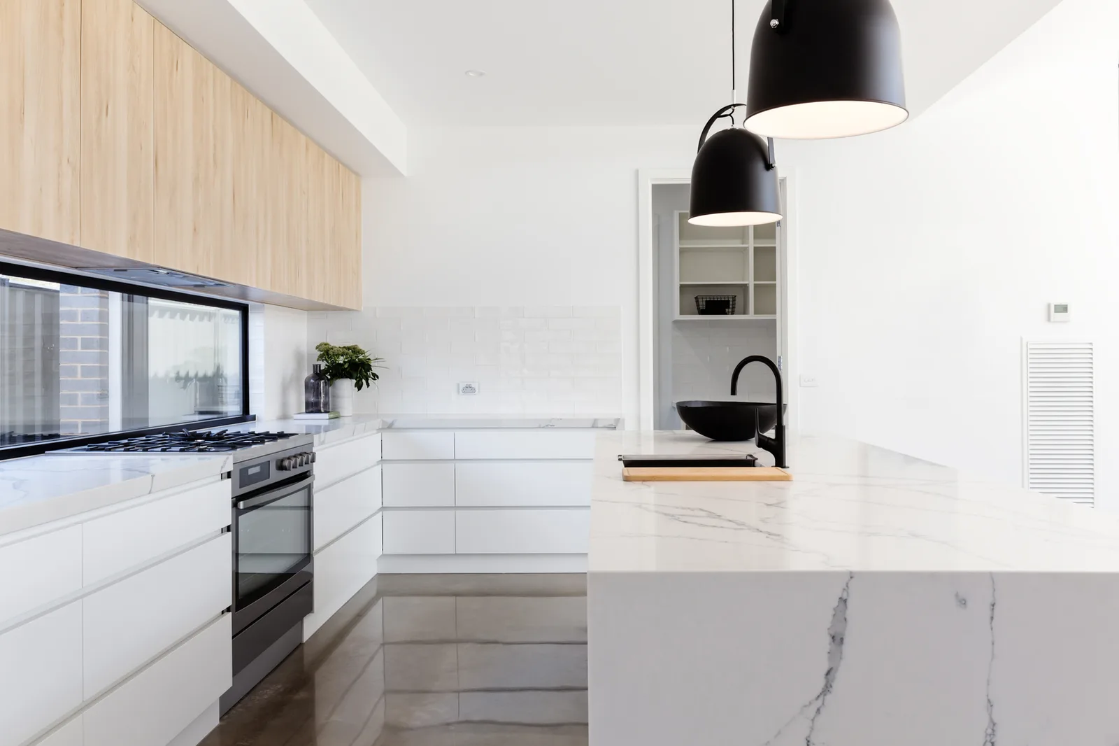 White kitchen with a marble island and a small window beside the range