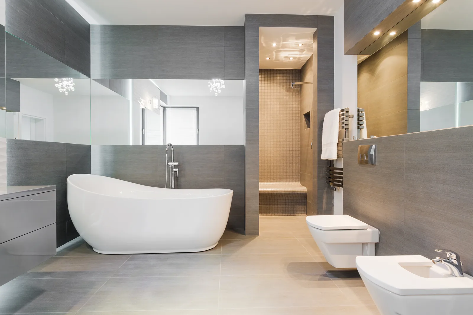 Grey-tiled bathroom with a freestanding tub and an obscured window