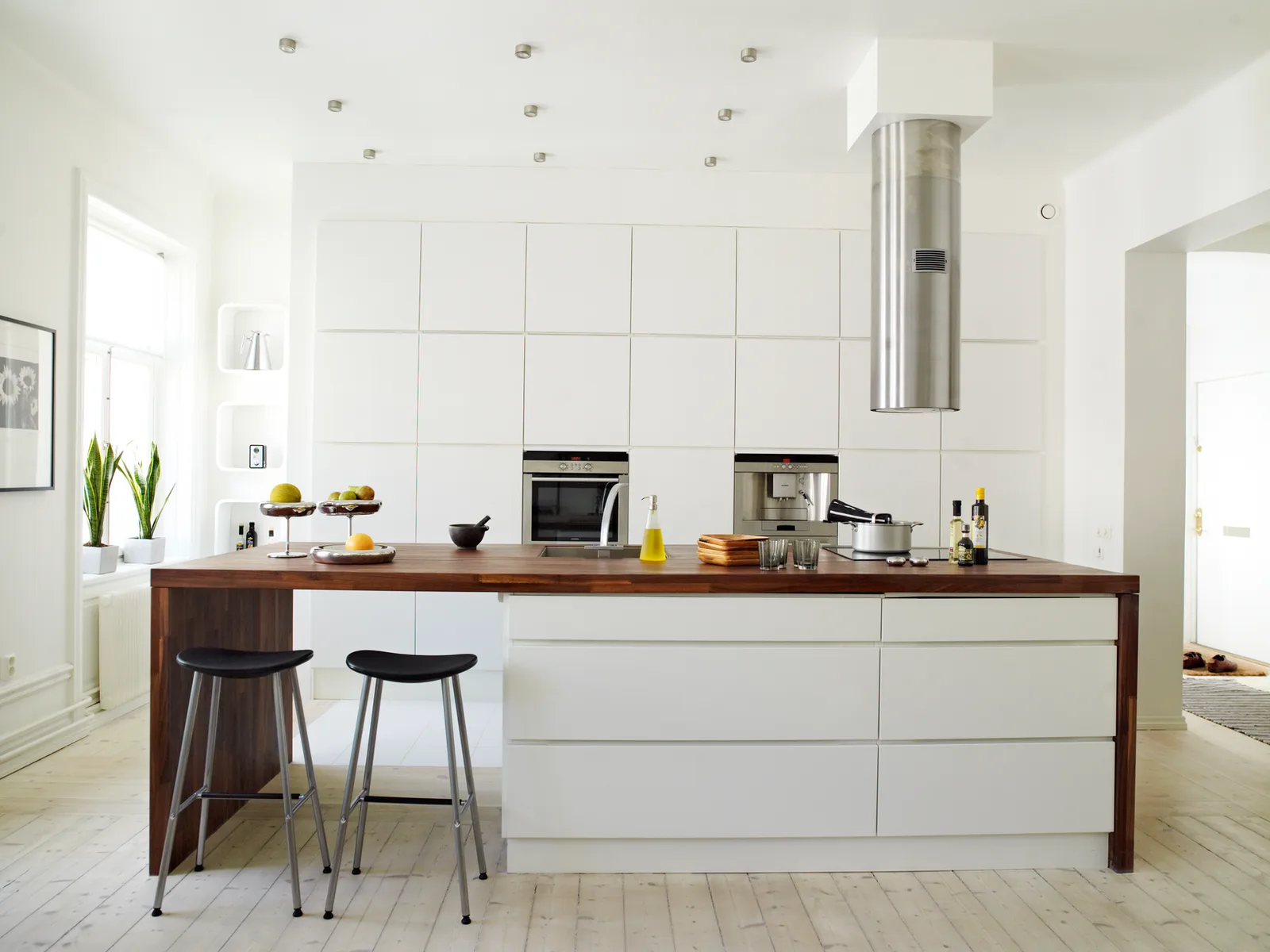 Minimal white kitchen with a walnut counter and a window above the sink