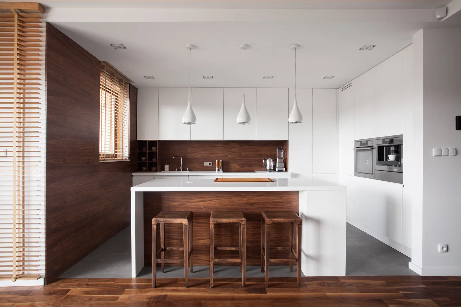 Wooden blind above a kitchen counter, slats angled to soften the light on a walnut wall